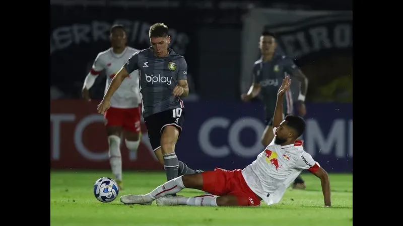 Cầu thủ của Platense với chiếc áo đỏ đang cố gắng chặn đứng đối thủ từ Deportivo Riestra với chiếc áo vàng và đen. Cầu thủ của Platense với chiếc áo đỏ đang cố gắng chặn đứng đối thủ từ Deportivo Riestra…